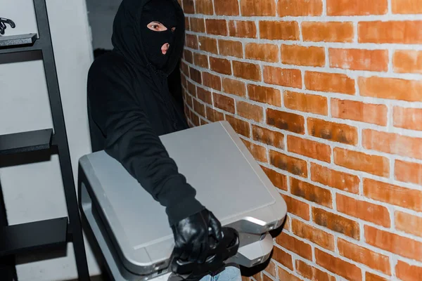Thief in leather glove and balaclava holding wireless speaker during stealing — Stock Photo