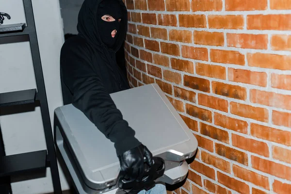 Dieb mit Lederhandschuhen und Sturmhaube hält beim Diebstahl Funklautsprecher in der Hand — Stockfoto