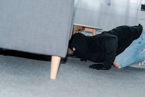 Side view of robber in mask and leather gloves looking under couch — Stock Photo