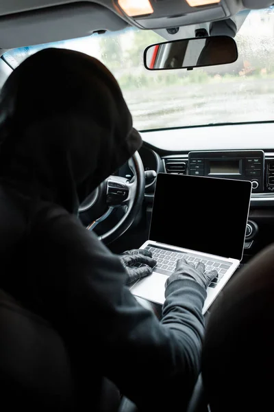 Back view of burglar in leather gloves using laptop with blank screen in auto — Stock Photo