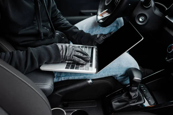 Vista recortada de ladrón en guantes de cuero usando el ordenador portátil con la pantalla en blanco en auto - foto de stock