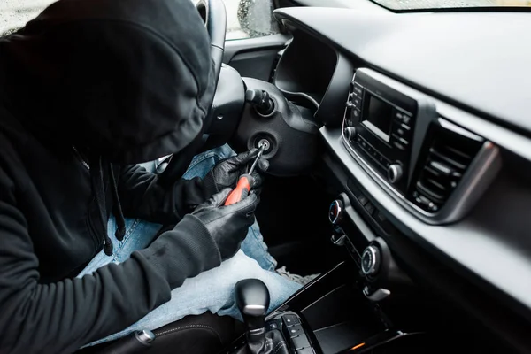 Enfoque selectivo del ladrón que sostiene el destornillador cerca de la cerradura de encendido en el coche - foto de stock
