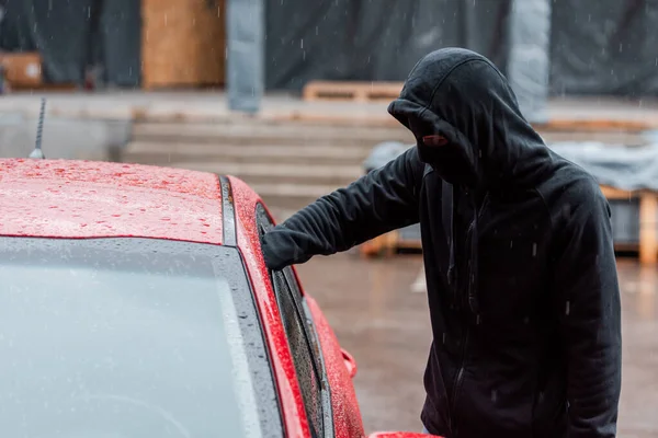 Theft in balaclava standing near car during robbery on urban street — Stock Photo