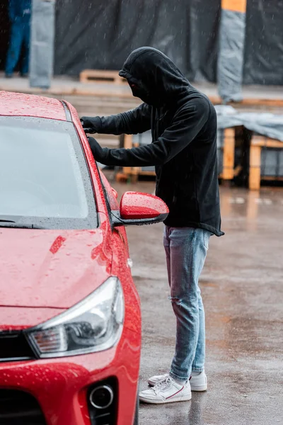 Selective focus of robber stealing car during rain on urban street — Stock Photo