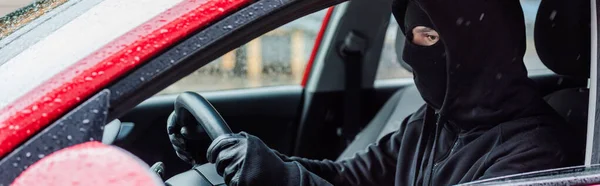 Panoramic crop of robber in balaclava sitting in auto during rain — Stock Photo