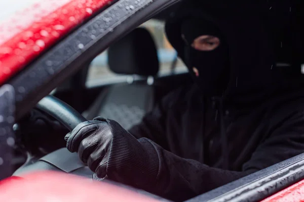 Foco seletivo de ladrão em balaclava e luva de couro sentado em carro — Fotografia de Stock