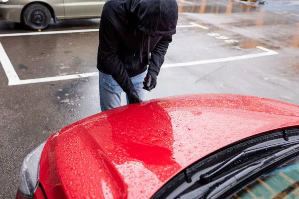 Robber in leather gloves holding screwdriver and opening car hood on urban street — Stock Photo