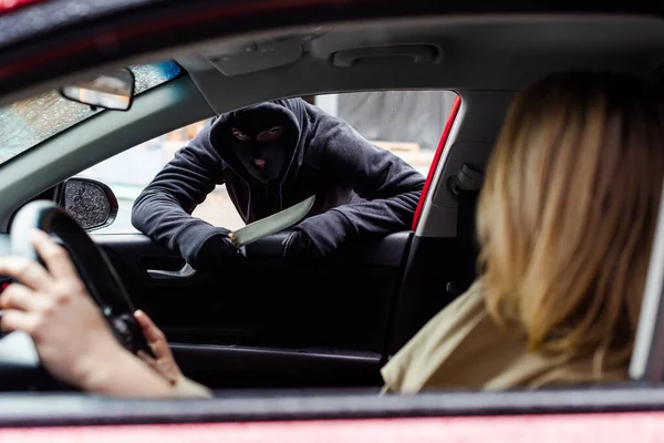 Selective focus of robber holding knife near woman sitting in auto during theft — Stock Photo