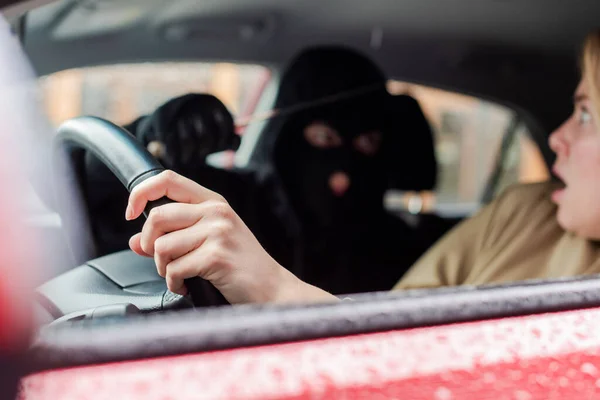 Selective focus of scared driver looking at robber with knife in car — Stock Photo