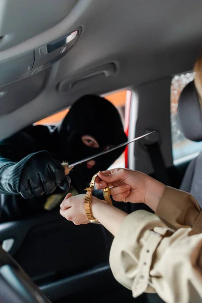 Selective focus of thief holding knife near woman taking off wristwatch in car — Stock Photo