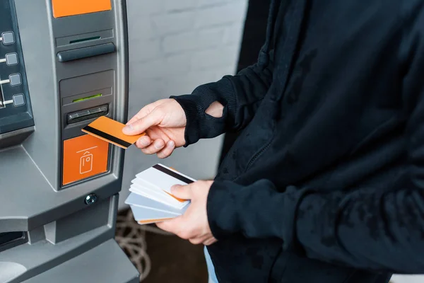 Vista recortada de ladrón con tarjetas de crédito cerca de cajero automático - foto de stock
