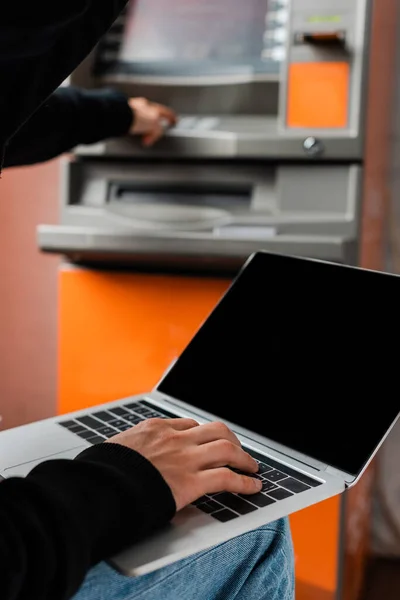 Enfoque selectivo del ladrón utilizando el ordenador portátil mientras se rompe la máquina de cajero automático - foto de stock