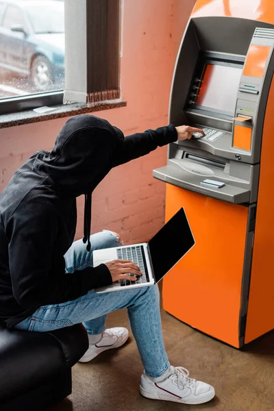 Vue latérale du cambrioleur à l'aide d'un ordinateur portable et d'un distributeur automatique pendant le vol — Photo de stock