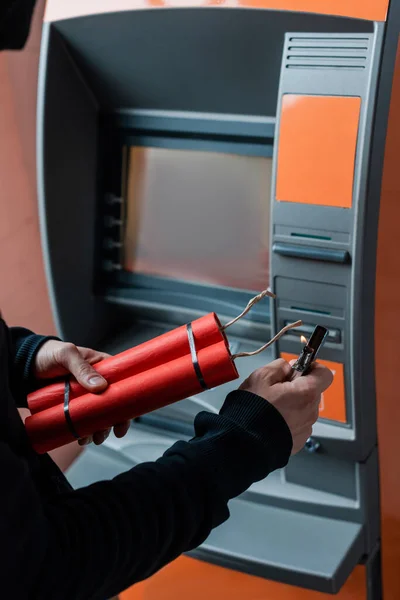 Обрезанный вид грабителя, держащего динамитовые палочки и зажигалку возле банкомата — стоковое фото