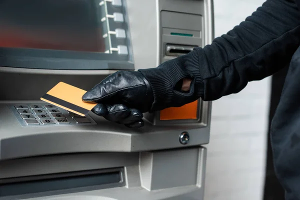 Обрезанный вид грабителя в кожаной перчатке с кредиткой возле банкомата — стоковое фото