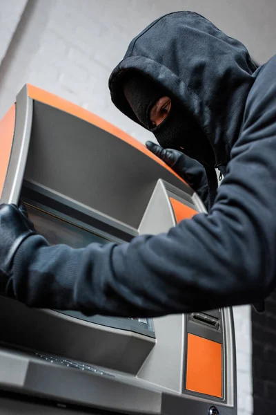 Low angle view of burglar in balaclava and lather gloves holding automated teller machine — Stock Photo