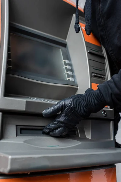 Vista cortada de ladrão em luva de couro segurando mão perto de dispensador de dinheiro de ATM — Fotografia de Stock