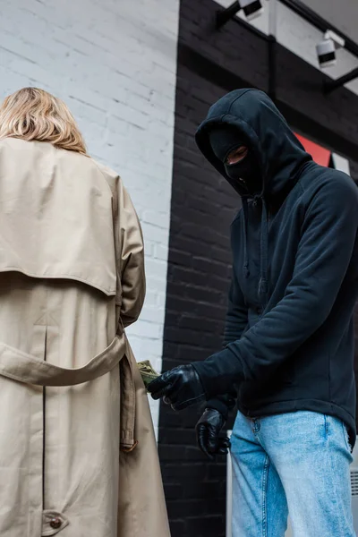 Vue à angle bas du voleur dans la cagoule tenant de l'argent près de la femme — Photo de stock