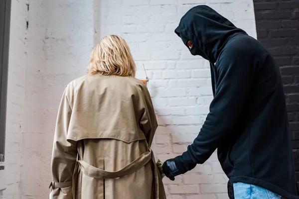 Robber in mask taking money from pocket of female coat — Stock Photo