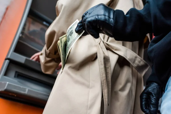 Tiefer Blickwinkel auf Dieb mit Lederhandschuhen, der Dollars in der Nähe von Frau im Mantel mit Geldautomat hält — Stockfoto