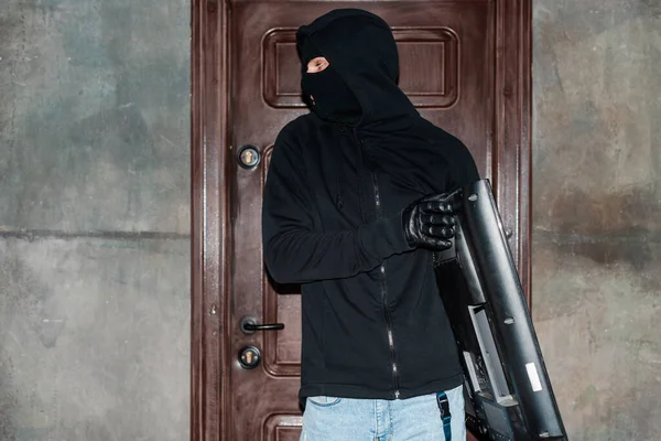 Robber en cagoule tenant la télévision près de la porte de la maison — Photo de stock