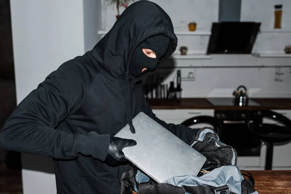 Robber en cagoule mettre un ordinateur portable dans un sac pendant le vol — Photo de stock