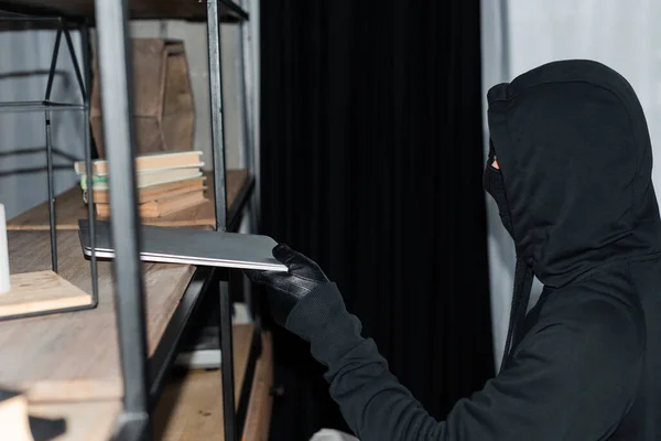 Вид збоку грабіжника, який бере ноутбук з шафи під час пограбування — стокове фото