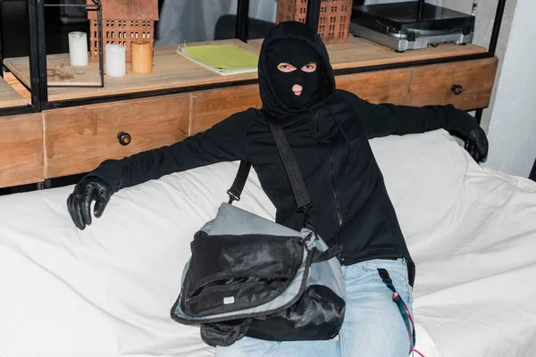 Robber en cagoule regardant la caméra alors qu'il était assis près d'un ordinateur portable dans un sac — Photo de stock