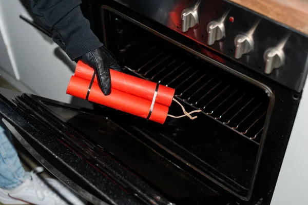 Cropped view of thief in leather glove putting dynamite in stove — Stock Photo