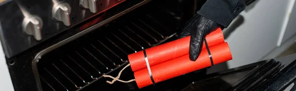 Panoramic shot of thief in leather glove putting dynamite in stove in kitchen — Stock Photo