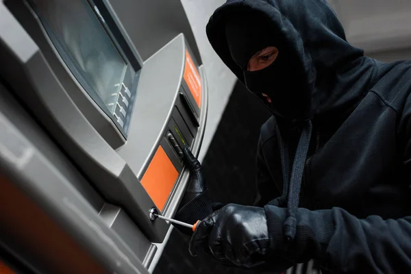 Low angle view of thief in balaclava using screwdriver while breaking atm — Stock Photo