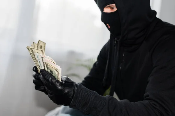 Вид сбоку грабителя в балаклаве с долларовыми банкнотами — стоковое фото