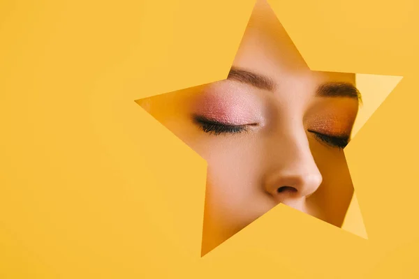 Retrato de mulher bonita com maquiagem brilhante no buraco em forma de estrela de papel com olhos fechados isolados no amarelo — Fotografia de Stock