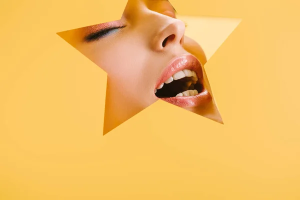 Portrait of beautiful woman with shiny makeup in paper star shaped hole with closed eyes and open mouth isolated on yellow — Stock Photo