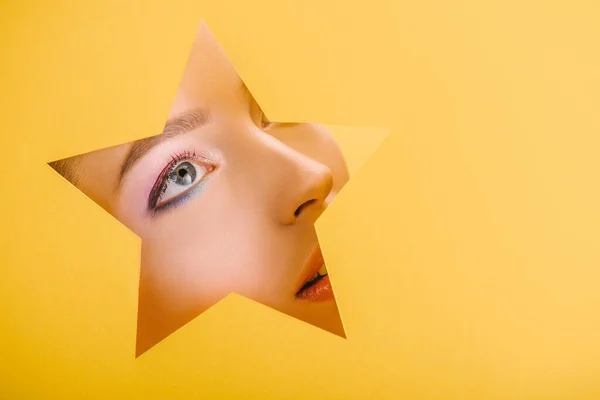 Portrait of beautiful woman with shiny makeup in paper star shaped hole looking up isolated on yellow — Stock Photo