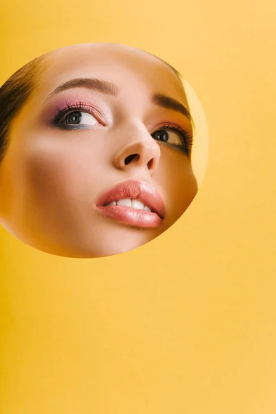 Retrato de mulher bonita com maquiagem brilhante em papel buraco redondo olhando para longe isolado no amarelo — Fotografia de Stock
