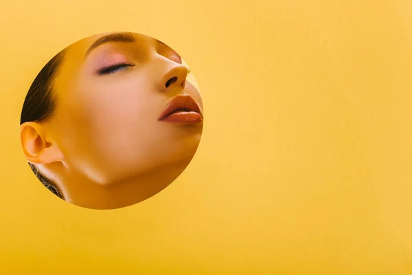 Портрет красивої жінки з блискучим макіяжем в паперовому круглому отворі з закритими очима ізольовані на жовтому — стокове фото