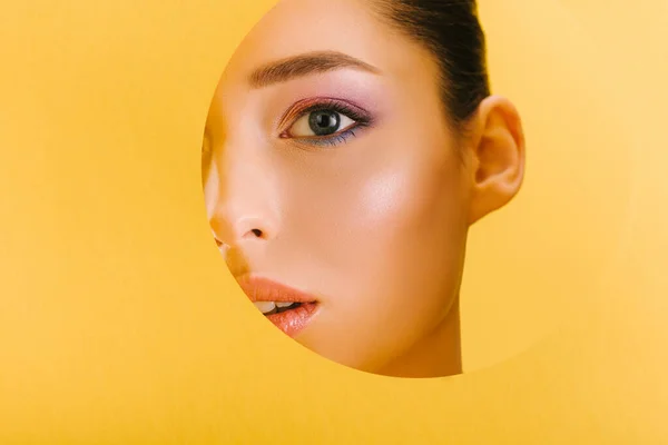 Retrato de mulher bonita com maquiagem brilhante em papel buraco redondo olhando para a câmera isolada no amarelo — Fotografia de Stock