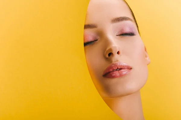 Portrait of beautiful woman with shiny makeup in paper round hole with closed eyes isolated on yellow — Stock Photo