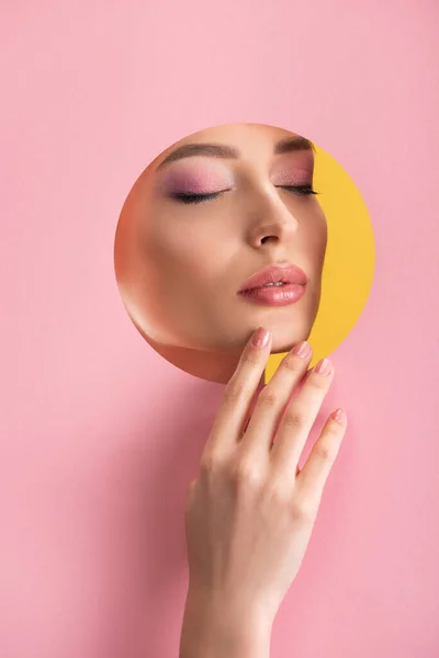 Ritratto di bella donna con trucco lucido in carta rosa foro rotondo con mano e occhi chiusi isolati su giallo — Foto stock