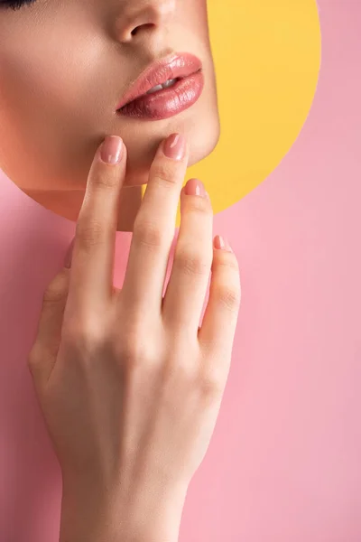 Partial view of beautiful woman with shiny lips in pink paper round hole with hand isolated on yellow — Stock Photo