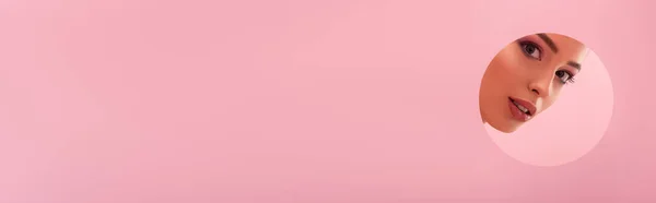 Portrait de belle femme au maquillage brillant dans un trou rond en papier isolé sur fond rose, prise de vue panoramique — Photo de stock
