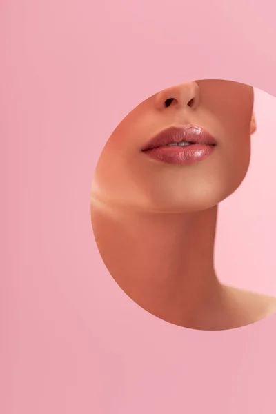 Частковий вигляд красивої жінки з блискучими губами в паперовому круглому отворі ізольовані на рожевому — стокове фото