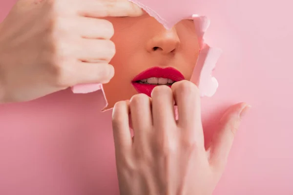 Обрізаний вид красивої жінки з малиновими губами в паперовому розірваному отворі ізольовано на рожевому — стокове фото