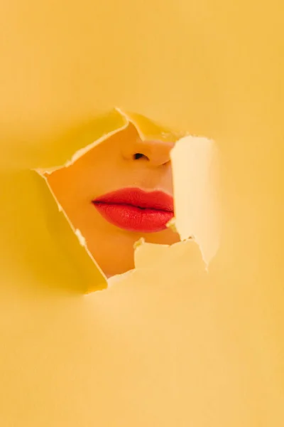 Vue recadrée de belle femme avec lèvres cramoisies en papier jaune trou déchiré — Photo de stock