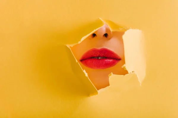 Vista recortada de hermosa mujer con labios carmesí en el agujero roto de papel amarillo - foto de stock