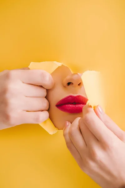 Vista recortada de hermosa mujer con labios carmesí en el agujero roto de papel amarillo - foto de stock