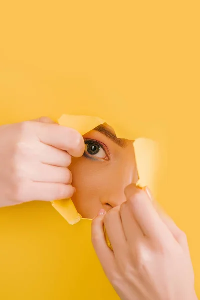 Vista recortada de la hermosa mujer mirando a través del agujero roto de papel amarillo - foto de stock
