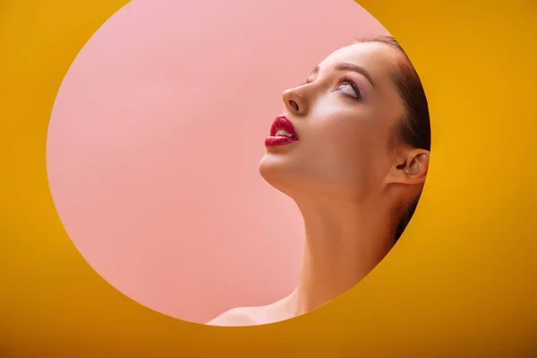 Naked beautiful woman with crimson lips looking up through yellow paper circle hole — Stock Photo