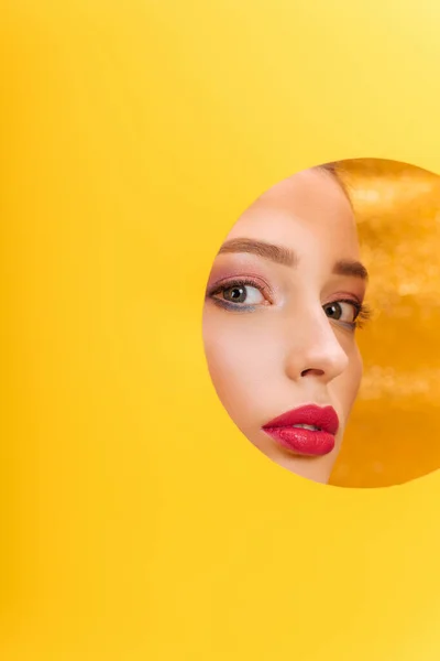 Schöne Frau mit buntem Make-up schaut durch gelbes Papierkreisloch — Stockfoto